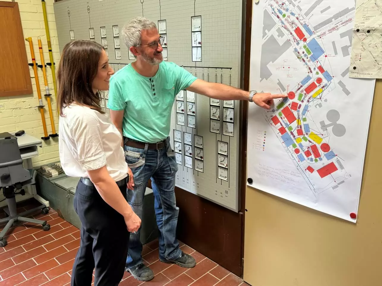 Fünf Personen stehen in einem modernen Besprechungsraum mit Konferenztisch, Stühlen und großem Bildschirm und präsentieren gemeinsam die technische Ausstattung des Raums.