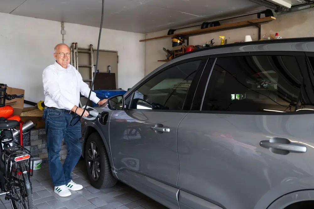 Mann steht an seinem E-Auto und lädt